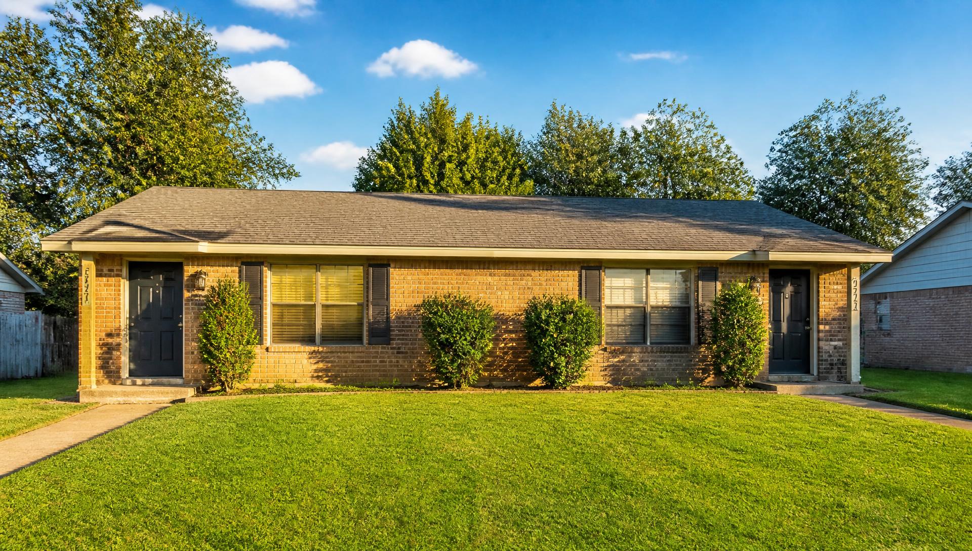 Brick rental duplex with a green lawn under a bright sky