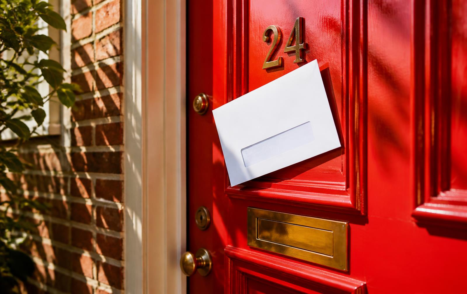 Formal notice envelope tucked into a vivid red front door